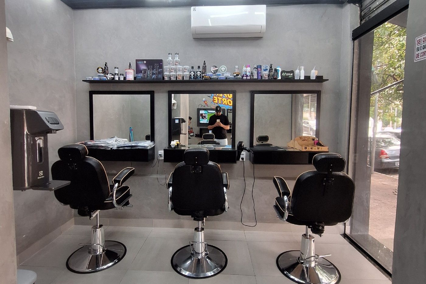 Espaço da New Style com três cadeiras, bancadas pretas e prateleira de produtos